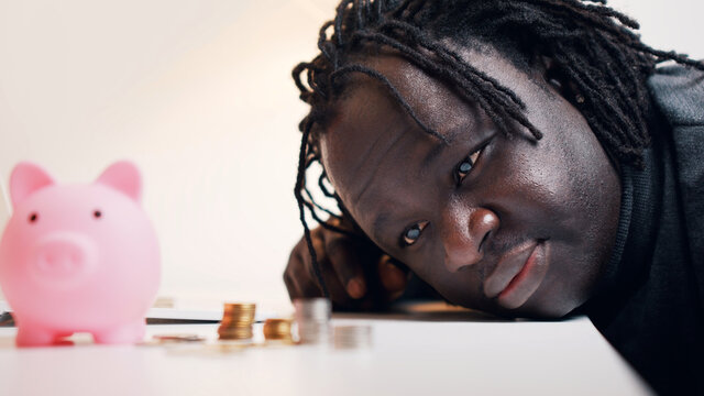 African american black man looking sad in the coins near the piggybank. High quality photo - Powered by Adobe