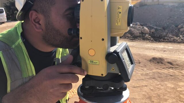 Land surveyor with tremor in hands works on geodetic total station. Geodetic engineer does measures stand working by theodolite at construction site.