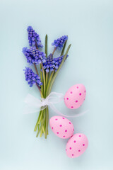 Easter greeting card with a bunch of bluebell flowers and pink festive Easter eggs against light blue or teal background. Springtime and Easter celebration concept