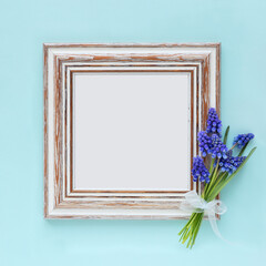 Hello Spring concept with a shabby chic empty frame and a bunch of bbluebells flowers against pale light blue or teal background. With plenty of copyspace for your text