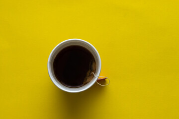 A disposable white cup full of tea, yellow background
