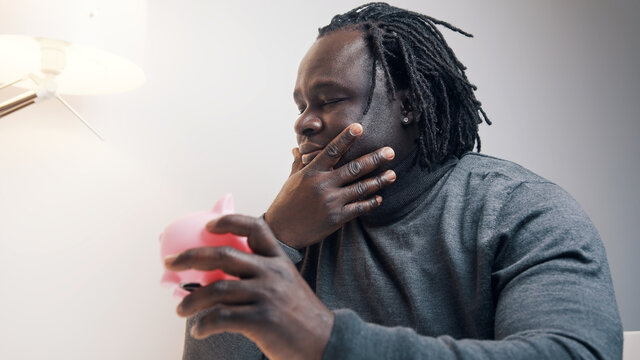 Bankruptcy Concept. Sad African American Black Man Looking At Empty Piggy Bank And Shaking His Head. High Quality Photo