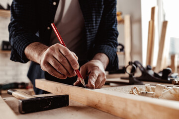 Carpenter makes pencil marks on a wood plank