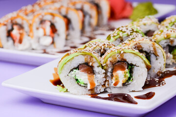 Eel, salmon and tuna sushi with unagi sauce served on a white plate over purple background.