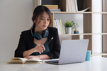 Young asian woman student e learning watching video training course sit at home office desk. girl look at laptop computer study with online teacher making notes.