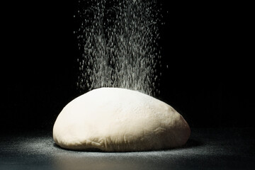 flour falls on the dough on a dark background.