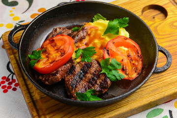 Close up of juicy beef steak served in a pan with bbq grilled tomatoes over traditional Ukrainian tablecloth.