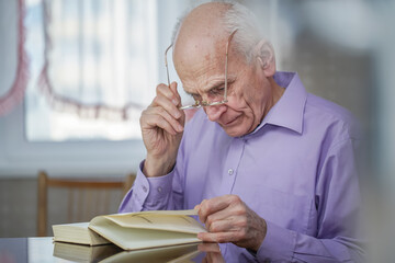 Grey haired elder citizen with glasses sitting at table of home or library