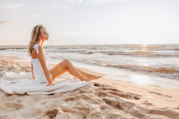 Fototapeta na wymiar Young slim woman walk alone on the beach or ocean and look at the horizont. Female wear white summer dress.