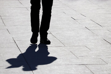 Black silhouette of slim man walking down the street, shadow on a pavement