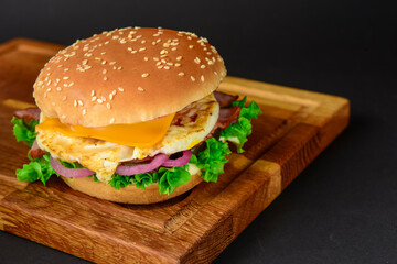 Bacon and beef patty burger with red onions and cheese over black background. Fast food, junk food concept.