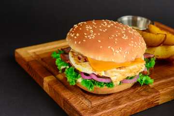 Bacon and beef patty burger with red onions and cheese over black background. Fast food, junk food concept.