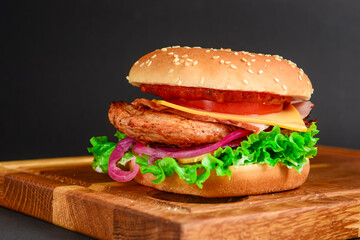 Bacon and beef patty burger with red onions and cheese over black background. Fast food, junk food concept.