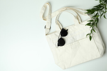 Blank textile bag, branch and sunglasses on white background