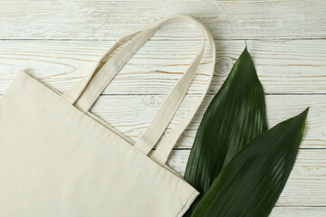 Eco bag and leaves on white wooden background