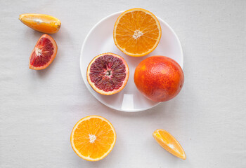 Flat lay of fresh sweet and juicy blood oranges and oranges, whole and cut on a white plate. Still life fruit photography.