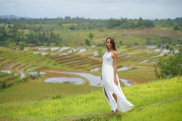 Fototapeta na wymiar Beautiful young woman in white vintage dress walking on rice fields in Asia. Girl travel and explore world. Romantic scene concept