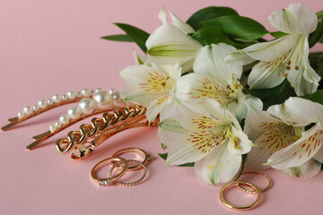 Jewelry and flowers on pink background, close up