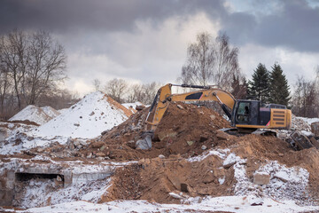 Fototapeta premium Excavator working at construction site. Backhoe digs ground for the foundation and for paving out sewer line. Construction machinery for excavating, loading, lifting and hauling of cargo on job sites