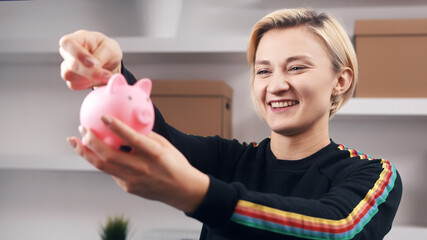 Savings concept. Happy caucasian blond woman pitting coins into the piggy bank. High quality photo