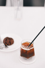 Black coffee on a white table top with a blurry chocolate cookie in the background.