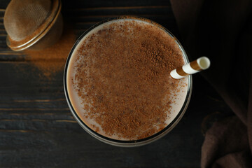 Glass of chocolate milkshake, kitchen towel and sieve on wooden table