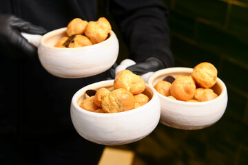 Tasty eclairs served in small white ceramic bowls by waiter in restaurant or cafe. Delicious dessert.