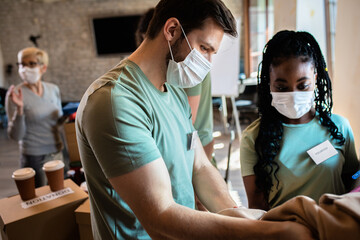 Group of volunteers with face mask working in community charity donation center.
