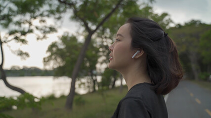 asian sport woman notification  from smart watch and answering phone call via wireless earphone at green lake park. female in sportswear talking and hangup phone call by tapping. technology digital.