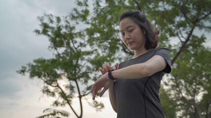 asian athlete woman using sport smart watch green nature park in evening sunset. female in sportswear touching screen application tracking activity and music. enjoy personal record data performance.