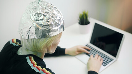 Crazy woman typing on laptop with foil hat to shields her from 5G waves, internet, electromagnetic...