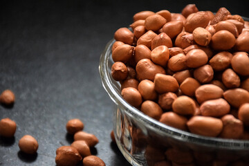 Stock photo of a brown color raw peanuts in transparent glass bowl, kept on black granite stone under natural light in kitchen. focus on object.
