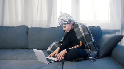 Fearful young woman with aluminum hat browsing social media. Conspiracy theory about 5g network...