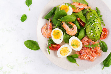 Ketogenic diet breakfast. Salt salmon salad with boiled shrimps, prawns, tomatoes, spinach, eggs and avocado. Keto, paleo lunch. Top view, overhead