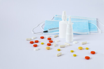 Multi-colored tablets and ampoules, vials of medicine, a syringe, medical masks on a white...