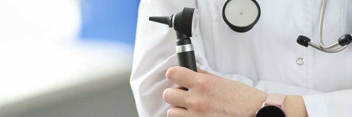 Otorhinolaryngologist holding otoscope in his hands in clinic closeup