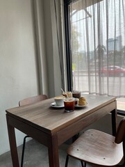 Coffee and dessert on the wood table beside the window and white curtain. Cafeteria concept