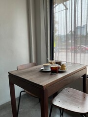 Coffee and dessert on the wood table beside the window and white curtain. Cafeteria concept
