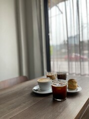 Coffee and dessert on the wood table beside the window and white curtain. Cafeteria concept