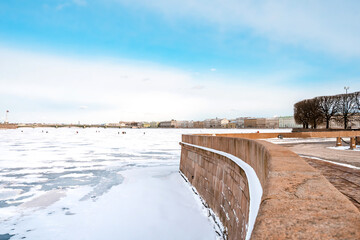 View of the Hermitage (Winter Palace) from the embankment of St. Petersburg from the icy Neva River, people walk along the river in early spring