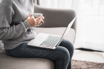 Naklejka premium women sitting relax on sofa holding coffee mug white with computer laptop at living room, new normal lifestyle, work from home concept.