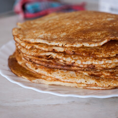 Stack of thin crepes, blini with butter on white plate. Maslenitsa, Shrove Tuesday concept. Vertical orientation, rustic style