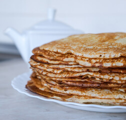 Stack of thin crepes, blini with butter on white plate. Maslenitsa, Shrove Tuesday concept. Vertical orientation, rustic style