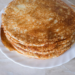 Stack of thin crepes, blini with butter on white plate. Maslenitsa, Shrove Tuesday concept. Vertical orientation, rustic style