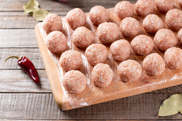 Side view closeup on raw semi-finished frozen meatballs on the wooden board with rice, onion and meat, horizontal