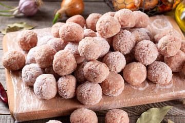 Side view closeup on raw semi-finished frozen meatballs on the wooden board with rice, onion and...