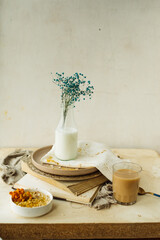 stylish simple monochrome beige table setting at home. gypsophila in glass bottle of milk on stack of old books, cup of coffee, plate of oatmeal, cotton napkins. creating comfort in interior