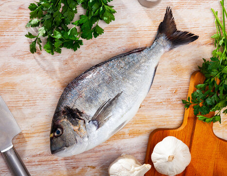 Uncooked dorado fish with lemon, garlic and parsley on wooden table. High quality photo