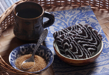 Coffee in a cup, chocolate chip cookies and brown sugar in a blue bowl on a wooden table close-up