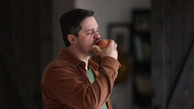man eating an apple near a window at home in a morning